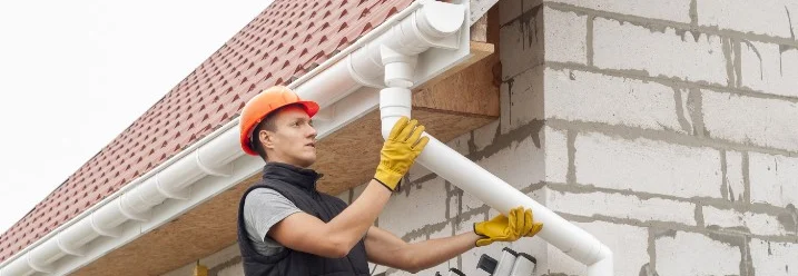 Person montiert Dachrinne an Hauswand.